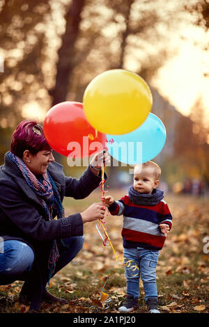 Little Boy. Infanzia felice. piccolo bambino ragazzo con un mucchio di palloncini nelle loro mani in Giallo autunno park. La famiglia. Foto Stock