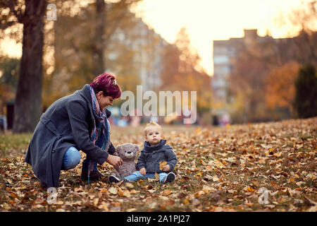 Madre bambino ragazzo giocando, sorridente e divertirsi in autunno il parco della città. Di colore giallo brillante e alberi e foglie Foto Stock