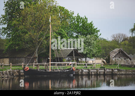 Legno vecchio viking capanne in un villaggio con una nave ormeggiata presso la banca. Foto Stock