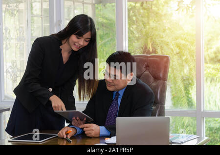 Amministratore. giovane bella femmina segretario mostra documento con mobile tablet e discussione sulla società di profitto per il senior boss in home office Foto Stock