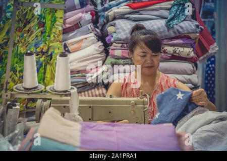 Chengdu, Cina - Luglio 2019 : donna cinese utilizza elettrico macchina da cucire per cucire vestiti nel suo negozio di tessuti Foto Stock