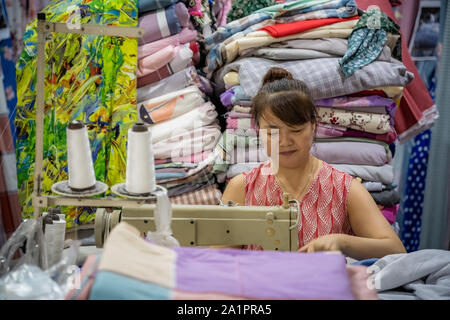 Chengdu, Cina - Luglio 2019 : donna cinese utilizza elettrico macchina da cucire per cucire vestiti nel suo negozio di tessuti Foto Stock