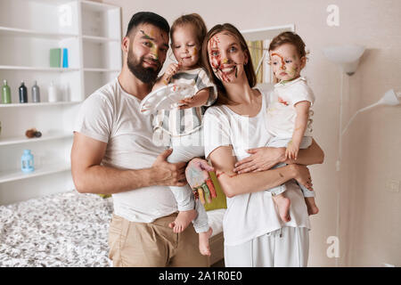 Positivi i giovani genitori mantenendo le loro belle figlie in mani in posa per la telecamera dopo la lezione di arte, hobby, tempo libero Foto Stock