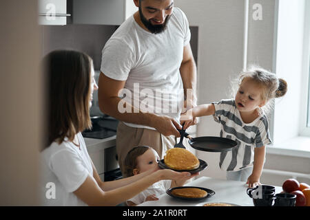 Bel piccolo bambino mettendo le frittelle sulla piastra, dando una mano per mamma e papà. close up foto Foto Stock