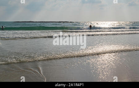 Silhouette di un uomo in piedi nel surf su una spiaggia di Tel Aviv in Israele con raggi del sole in background Foto Stock