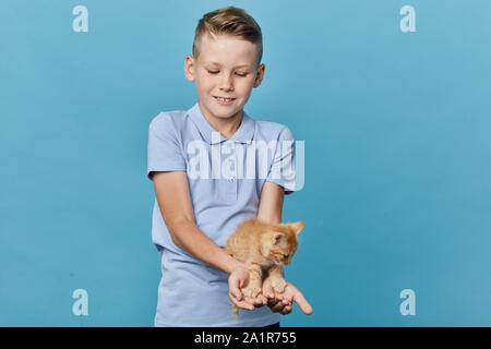 Felice piccolo ragazzo giocando con PET in ambienti chiusi, chiudere su ritratto, isolato sfondo blu, studio shot, passatempo Foto Stock