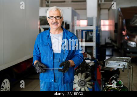 Maturo di successo proprietario della macchina il servizio di riparazione con tablet che vi guardano con sorriso mentre si lavora in hangar Foto Stock