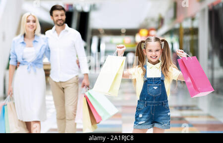 I genitori e la figlia eccitato il trasporto delle borse della spesa a piedi in centro commerciale Foto Stock