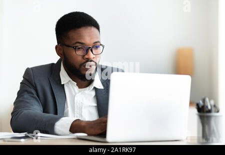 Grave imprenditore nero lavorando sul computer portatile in ufficio Foto Stock