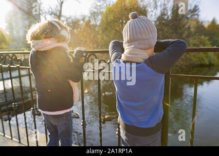 Bambini Un ragazzo e una ragazza dorsi permanente sul ponte, guardando le anatre, soleggiata giornata autunnale nel Parco, ora d'oro Foto Stock