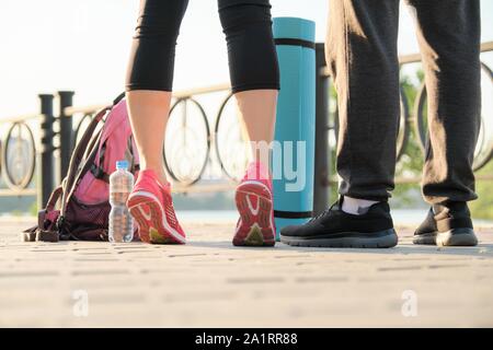 Un sano stile di vita atletico di un uomo e di una donna, ravvicinata di un paio di gambe in sneakers sportswear con bottiglia di acqua di esercizio mat Foto Stock