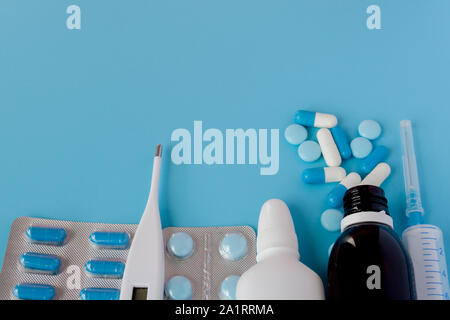 Il trattamento di raffreddori e influenza. Diversi medicinali, un termometro, spray da un naso chiuso e un dolore in una gola su uno sfondo blu. Spazio di copia Foto Stock