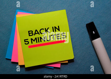 Torna in 5 minuti su foglietti adesivi isolata sulla scrivania in ufficio Foto Stock