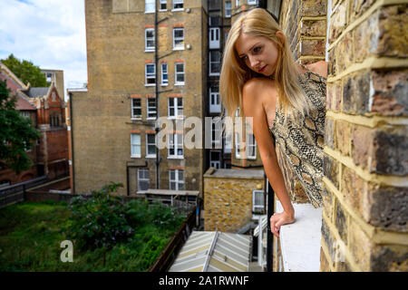 Ritratto di giovane donna con fiducia nei suoi occhi, guardando fuori della finestra di un vecchio edificio in mattoni e sperare per il meglio le cose a venire a Londra Foto Stock