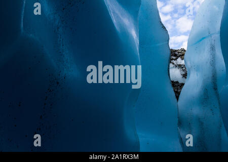 Guardando fuori una stretta entrata di una caverna di ghiaccio con blu scuro pareti all'interno del ghiacciaio Matanuska in Alaska. Foto Stock