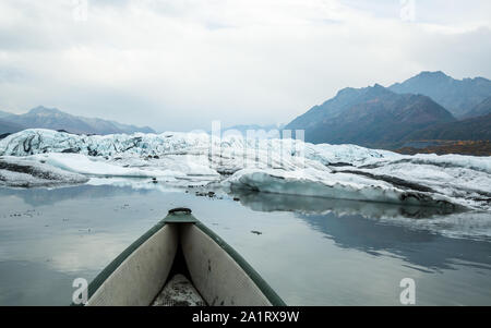 Il fumo riempie la valle Matanuska e nuvole di overhead per aggiungere la sensazione cupa. Un grigio e verde canoa galleggia in acqua calma sotto la Matanuska Glacie Foto Stock