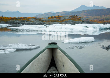 Al di sotto del ghiacciaio Matanuska, una canoa gonfiabile fluttua tra gli iceberg. Nella distanza, giallo dorato segnale lascia la fine dell'estate. Foto Stock