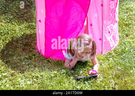 Bambina con la compressa è parzialmente in una tenda rosa all'aperto Foto Stock