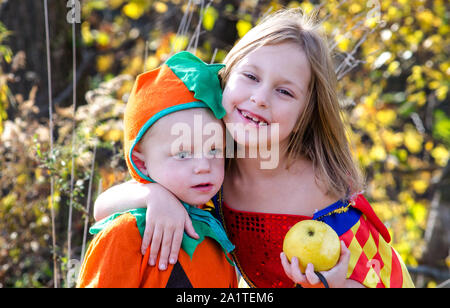 Un big sister abbraccia il suo piccolo fratello, entrambi posti in adorabili costumi di Halloween. Uno è una zucca e gli altri una principessa. Foto Stock