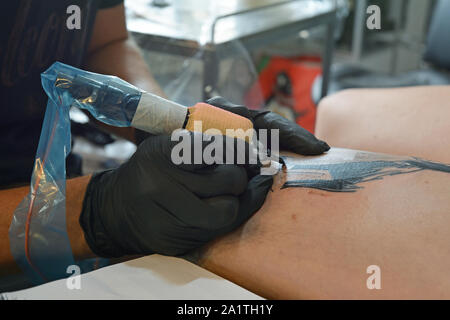 Close up del tatuaggio processo con le mani in guanti neri azienda tattoo machine avvolti in plastica Foto Stock