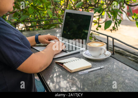 Asian utilizzando laptop mentre si gusta un caffè a una caffetteria esterna Foto Stock