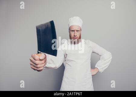 Ritratto di funky mad attraente bello butcher guy holding che mostra il coltello in mano braccio minaccioso pronto a preparare il piatto isolate su pastello grigio Foto Stock