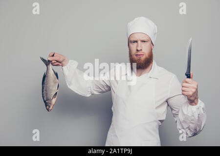 Ritratto di mad attraente bello grave fury butcher guy holding che trasportano il pesce e il coltello in mano braccio di frutti di mare gustosa ricetta golosa isolate su grigio Foto Stock