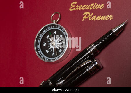 Angolo di visualizzazione di un colore rosso scuro executive planner con semplice bussola e penne Foto Stock