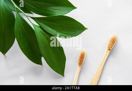 Eco Friendly di bamboo naturale spazzolini da denti su sfondo bianco con foglie verdi. Rifiuti Zero concetto, plastica libera Foto Stock