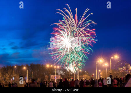 Molti residenti guarda la festosa fuochi d'artificio sopra la città di notte, rosso giallo e verde luci nel cielo blu scuro al di sopra della città Foto Stock