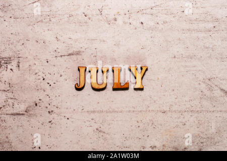 La parola luglio stabiliti nelle lettere di legno su uno sfondo luminoso. Close-up. Estate Tempo anni e mesi dell'anno Foto Stock