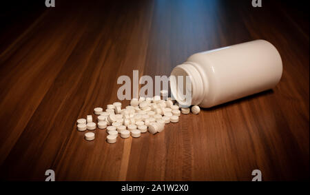 Le capsule di bianco pillola versato fuori dalla bottiglia di plastica bianca contenitore. Global Healthcare concetto. Antibiotici la resistenza al farmaco. Foto Stock
