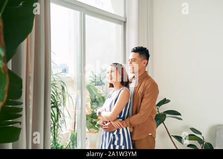 Romantico lieto coppia giovane in piedi e abbracciando insieme permanente, mentre dalla finestra Foto Stock