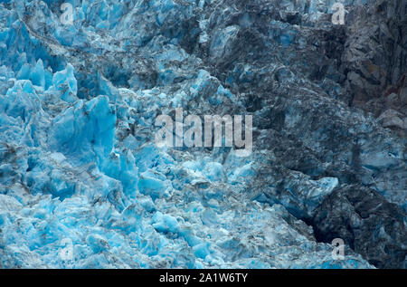 Grandi blocchi di ghiaccio dal ghiacciaio Northwest, intensamente blu o grigio di colore, accanto a massicce rocce. Foto Stock