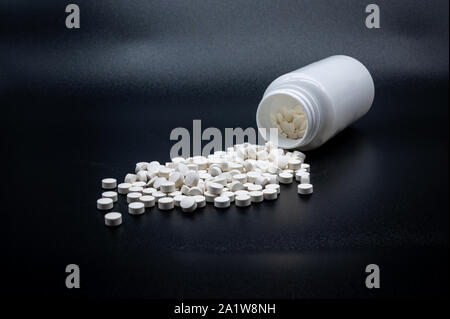 Un mucchio di pillole di bianco nella parte anteriore di una mezza bottiglia vuota Foto Stock