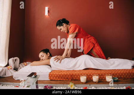 Massaggiatore asiatico facendo massaggio alla schiena di donna attraente in spa salone Foto Stock