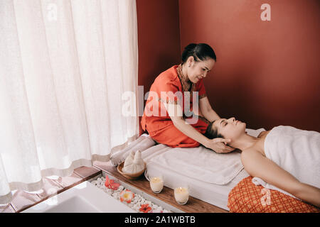 Massaggiatore asiatico facendo massaggio al collo per donna in spa salone Foto Stock