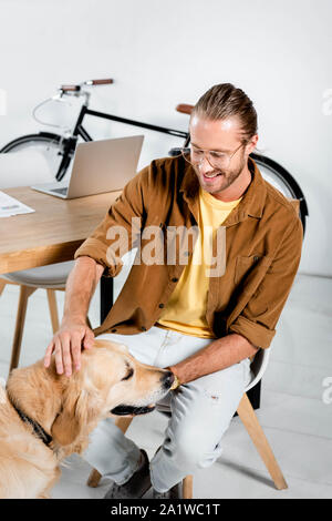 Sorridente e uomo bello accarezzare carino golden retriever in office Foto Stock