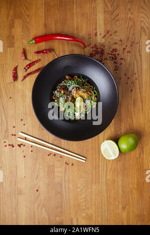 Al di sopra di vista sullo sfondo di un bellissimo piatto asiatico nel wok ciotola messa sul tavolo di legno decorato con peperoncino e lime, spazio di copia Foto Stock