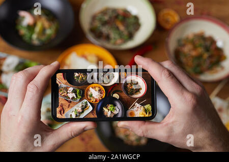 Close up di un irriconoscibile uomo prendendo foto dei deliziosi piatti asiatici, concentrarsi sulla schermata dello smartphone, spazio di copia Foto Stock