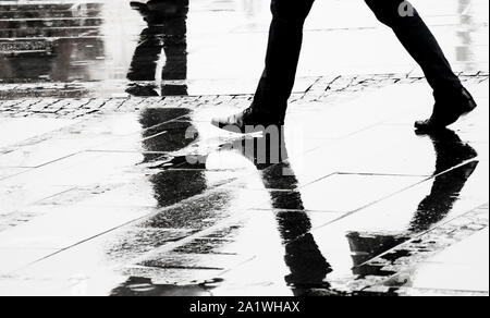 Silhouette e la riflessione di un uomo in eleganti scarpe umide a piedi via della città su s Rainy day, gambe in bianco e nero Foto Stock