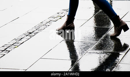 Silhouette ombra e riflesso di una donna in stivaletto scarpe umide a piedi via della città in un giorno di pioggia, soltanto sulle gambe Foto Stock