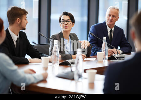 Ritratto di giovane imprenditrice intervenendo a una conferenza mentre a discutere di progetti e idee con i colleghi seduti al tavolo rotondo, spazio di copia Foto Stock