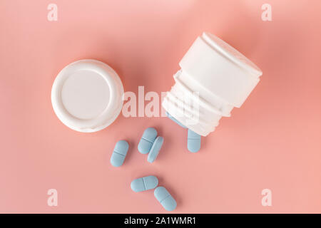 Medicina bianco bottiglia e pillole blu su sfondo rosa. Close-up. Foto Stock