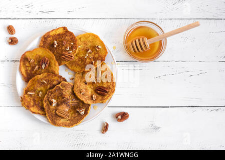 Frittelle di zucca con noci pecan e miele sul tavolo bianco, vista dall'alto, copia dello spazio. Tradizionale autunnale di sana colazione - Frittelle di zucca. Foto Stock