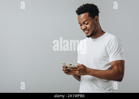 African American uomo conteggio banconote di dollari isolato su grigio Foto Stock