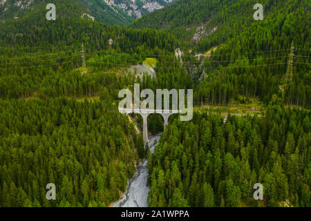 Inn fiume che scorre nella foresta in Svizzera. Vista aerea da fuco su un vecchio ponte ferroviario viadotto in montagna Foto Stock