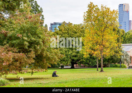 Ragazza solitaria rilassa seduto sull'erba nei bellissimi Giardini Fitzroy, zona centrale di Melbourne, Australia Foto Stock