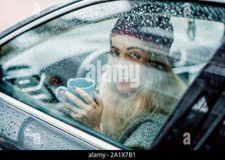 Giovane donna beve caffè e sorridente in auto. Foto Stock