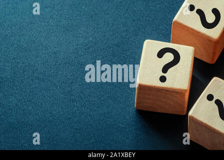 Bordo laterale dei punti interrogativi su cubi di legno su un blu scuro dello sfondo testurizzata con spazio di copia Foto Stock